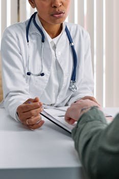 A doctor in a white coat consulting a patient at a table with medical documents.