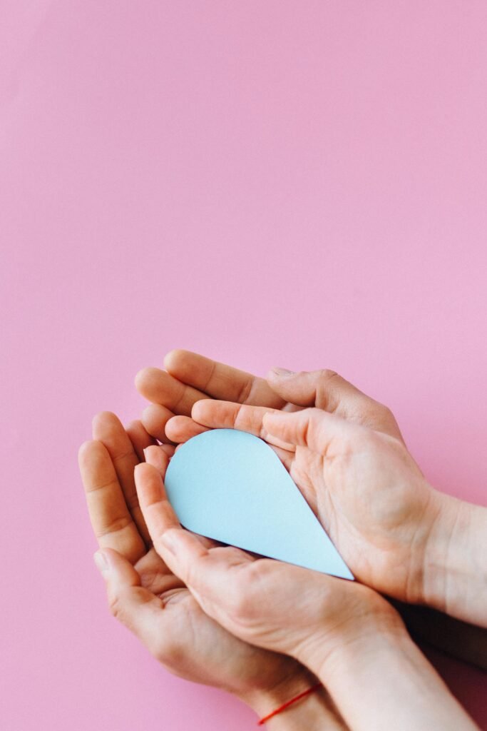 Close-up of hands holding a blue drop cutout symbolizing diabetes awareness on a pink background.